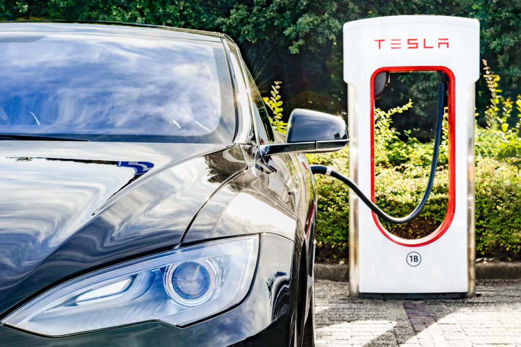 Zevenaar, Nederländerna – 10 september 2015: Svart Tesla Model S elbil vid en Tesla kompressorladdningsstation. Superchargers är gratis kontakter som laddar Model S på några minuter. Superchargers används för långväga resor, som ligger längs de mest populära rutterna i Nordamerika, Europa och Asien.